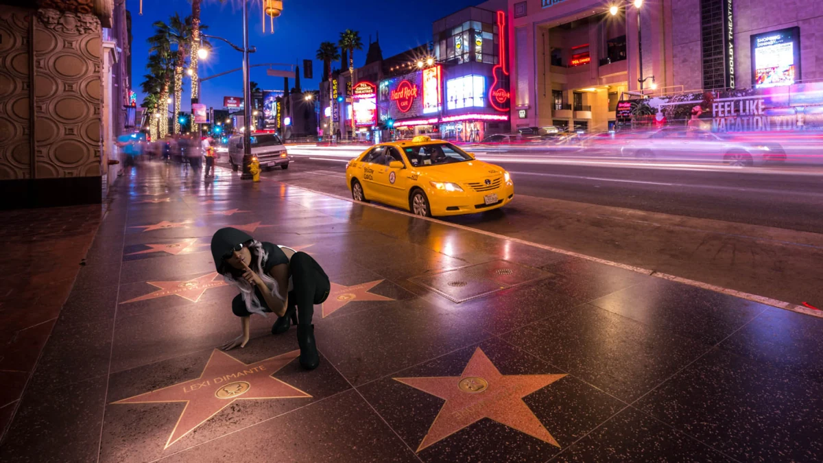 Two characters kneel beside a star on a brightly lit city pavement.